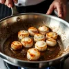 A chef searing scallops in a stainless steel pan
