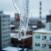 A detailed macro of a melting icicle with industrial buildings blurred in background