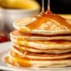 A stack of fluffy pancakes with maple syrup dripping