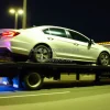 Car being towed on a flatbed truck at night city lights background