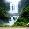 Car parked beside a massive waterfall mist in the air vibrant greenery