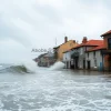 Sea level rise flooding an old coastal town waves crashing into historic buildings photojournalism